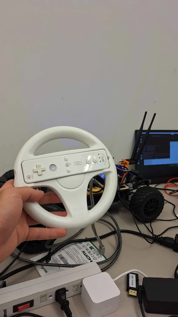 A person holding a Wii remote inside of a Wii wheel in front of a robotic car